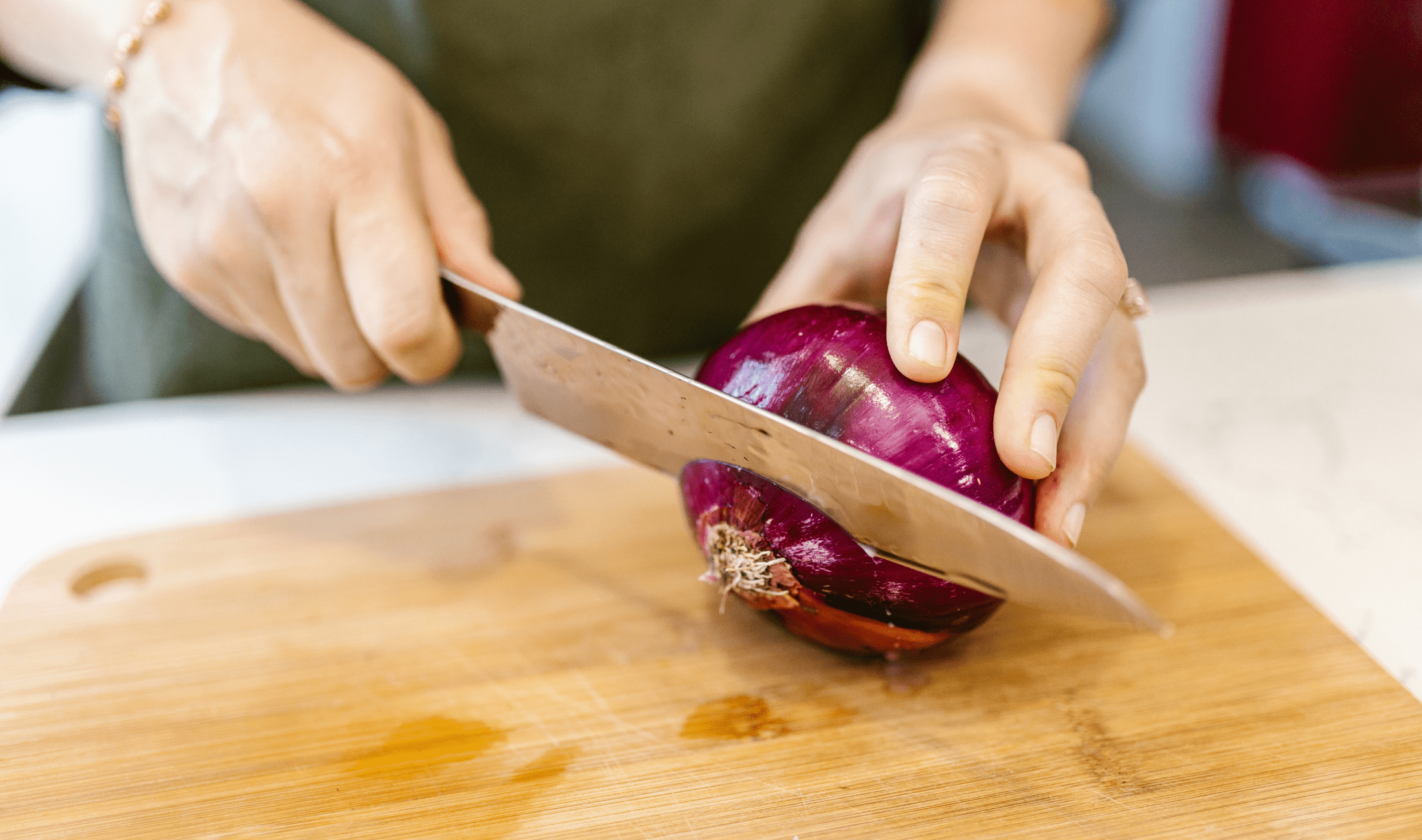 A hand cutting the root off an onion.