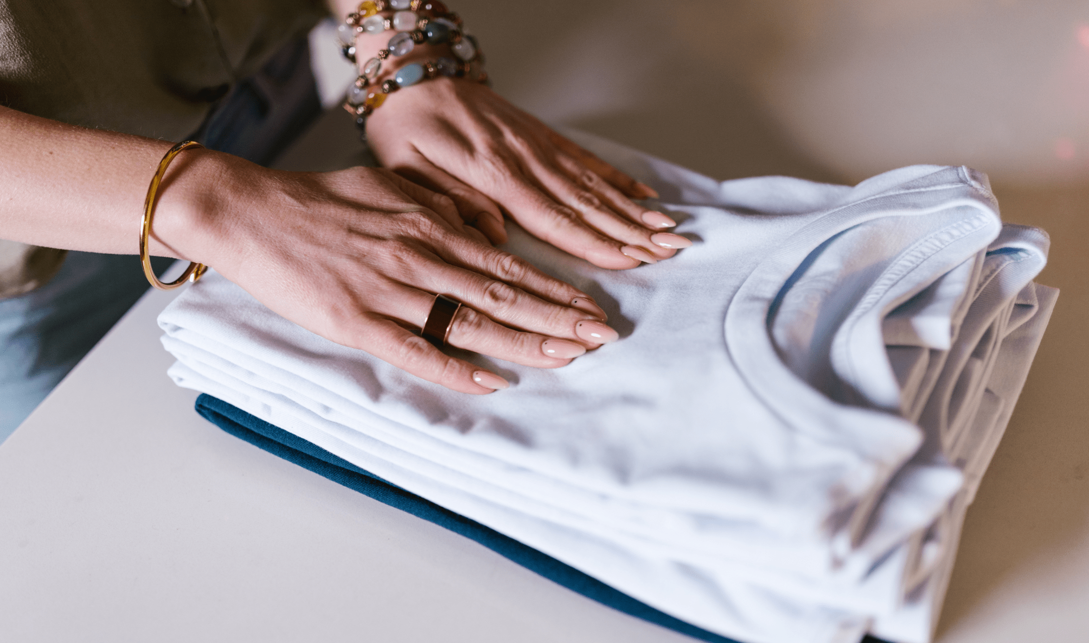 A pair of hands smoothing a stack of folded clothes.