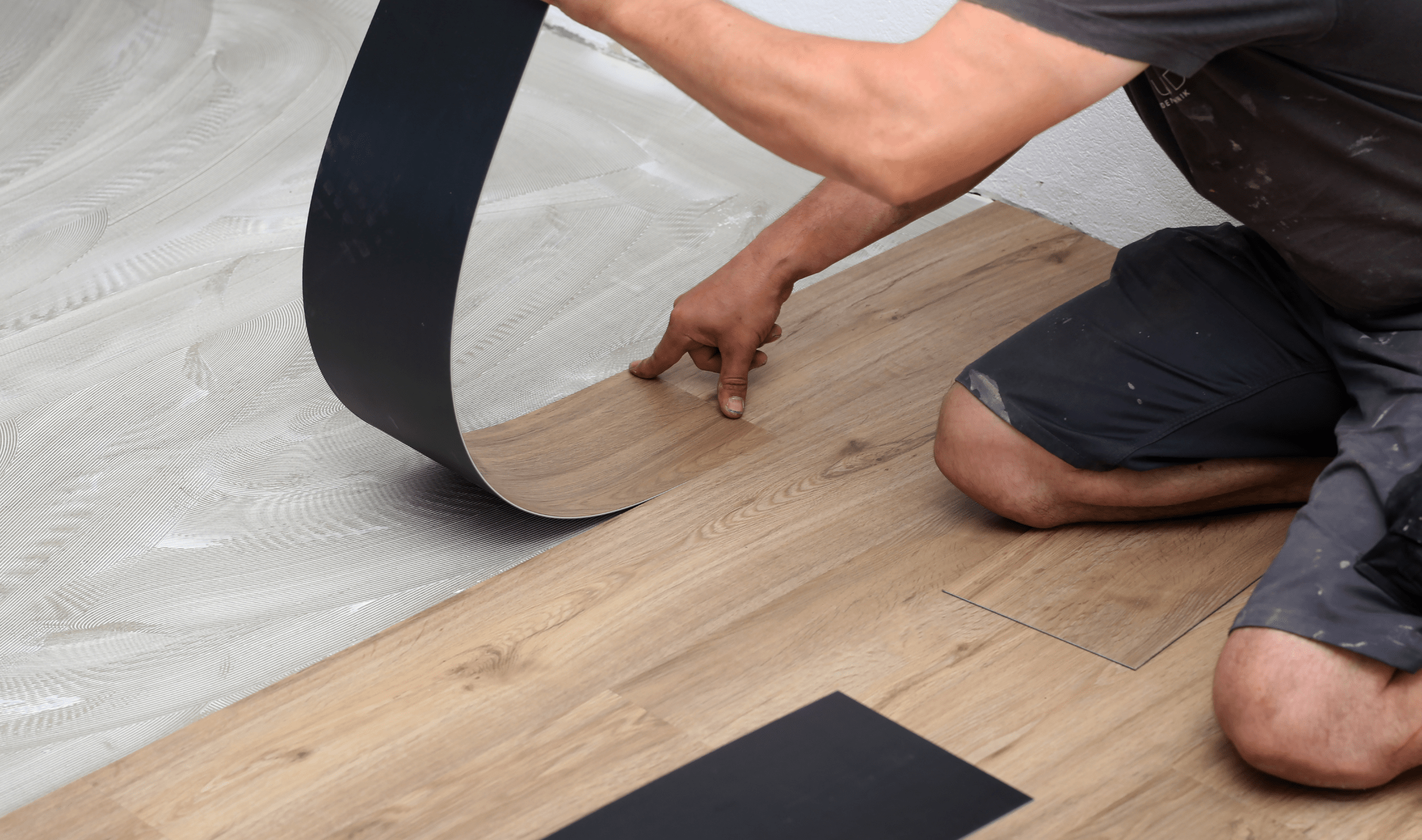 A pair of hands installing vinyl plank flooring.