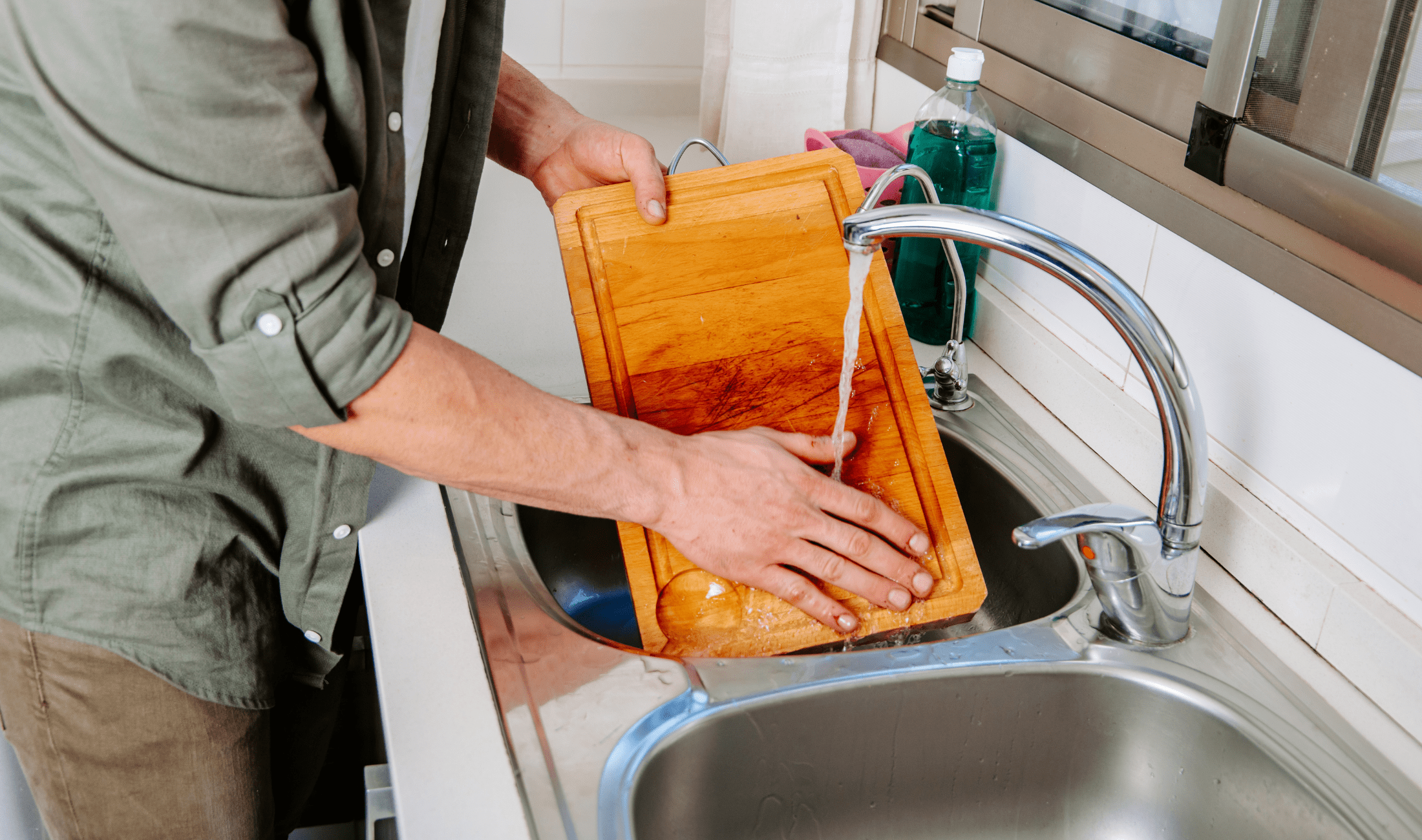 A person washing their cutting board with water in a sink.
