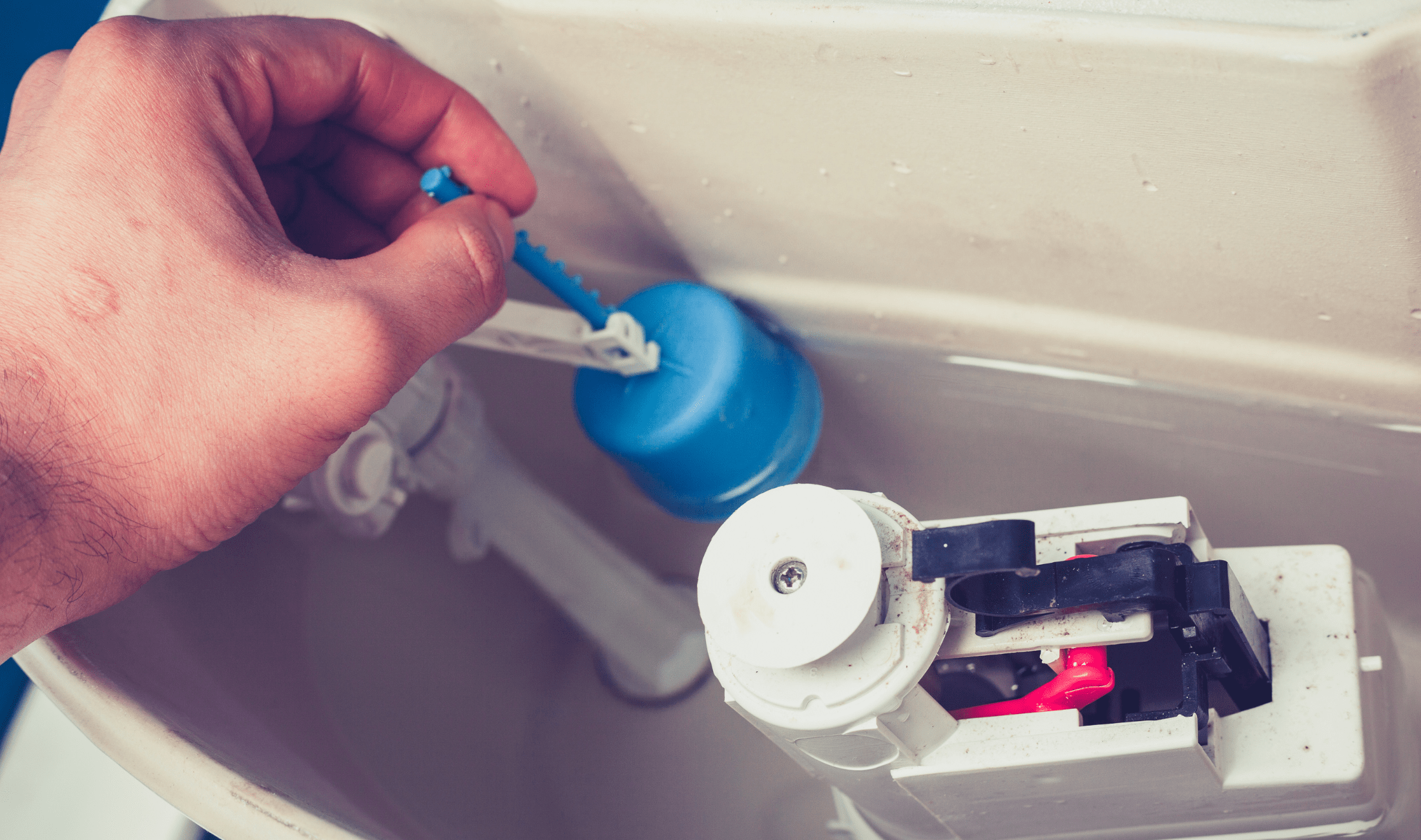 A person reaching into their toilet tank to fix the valve.