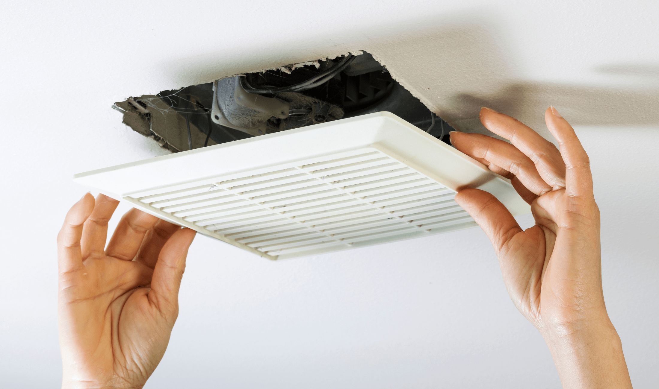 A pair of hands removing a vent cover from the ceiling.