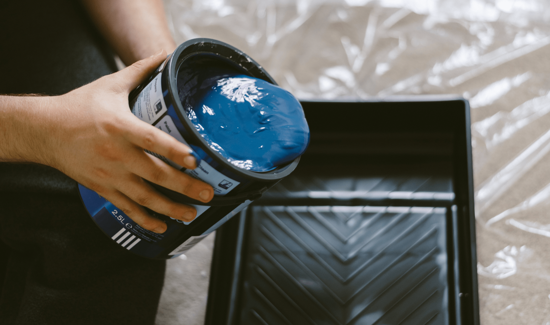 Someone pouring a can of blue paint into a tray.