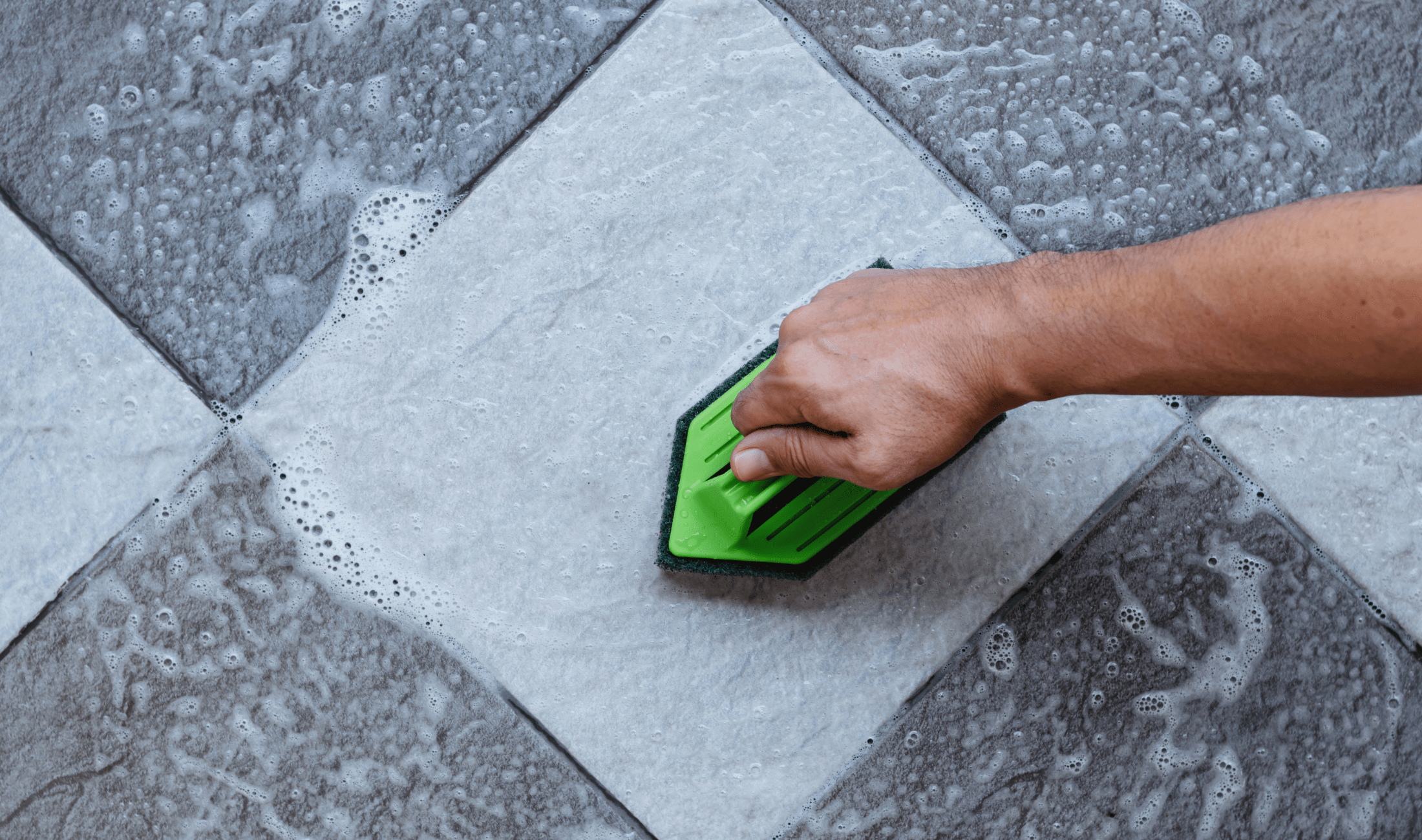 A hand scrubbing a tile floor with a brush.