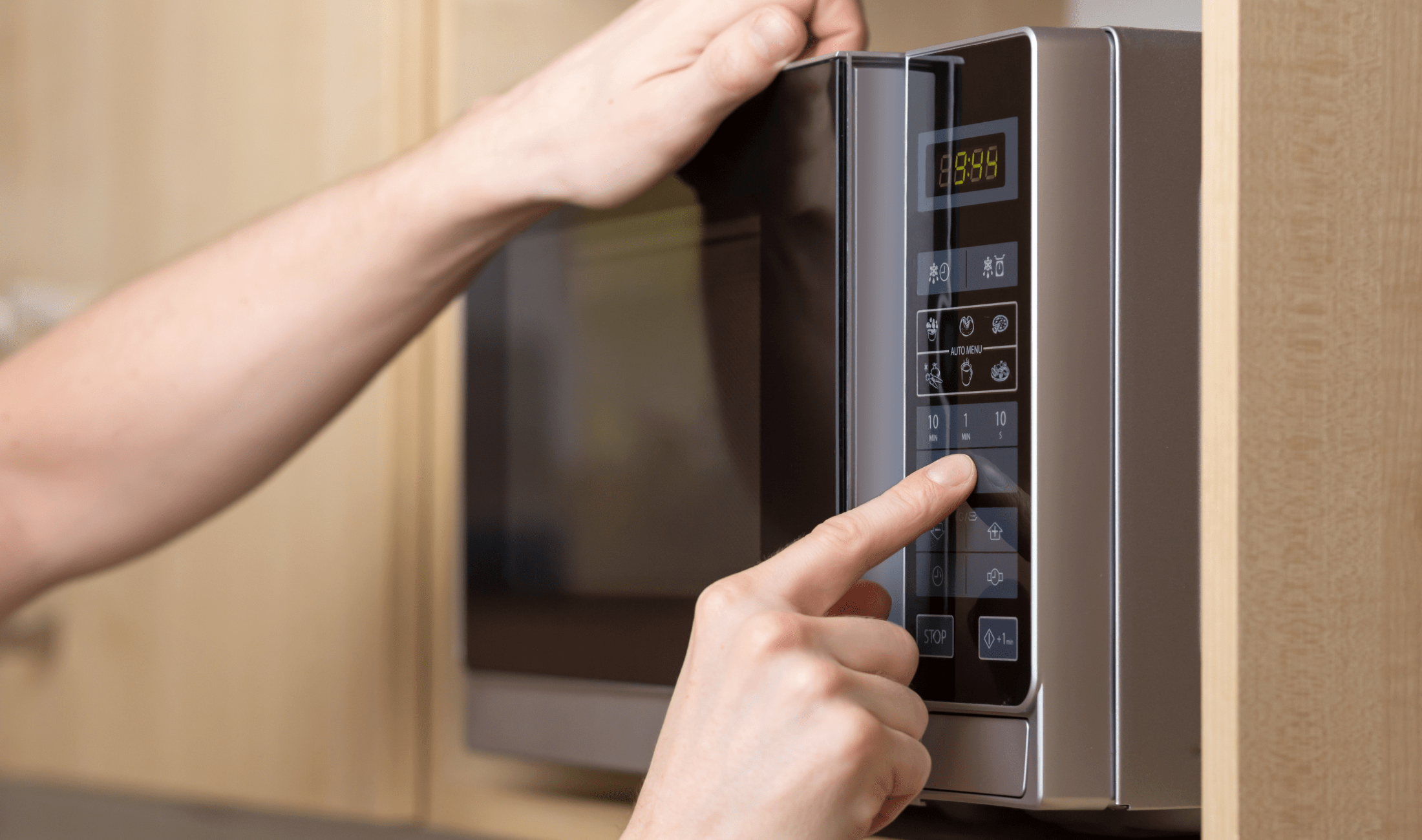 A hand reaching out to put numbers into a microwave.