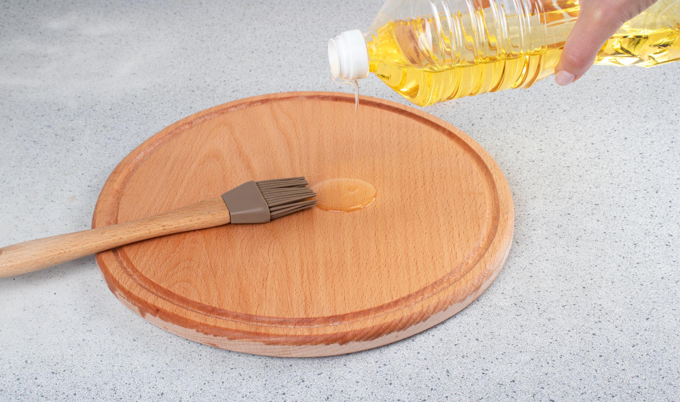 A person pouring oil on a cutting board that has a silicone oil brush on it.