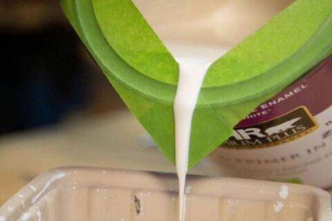 Pouring paint from can with green painter's tape used as spout.