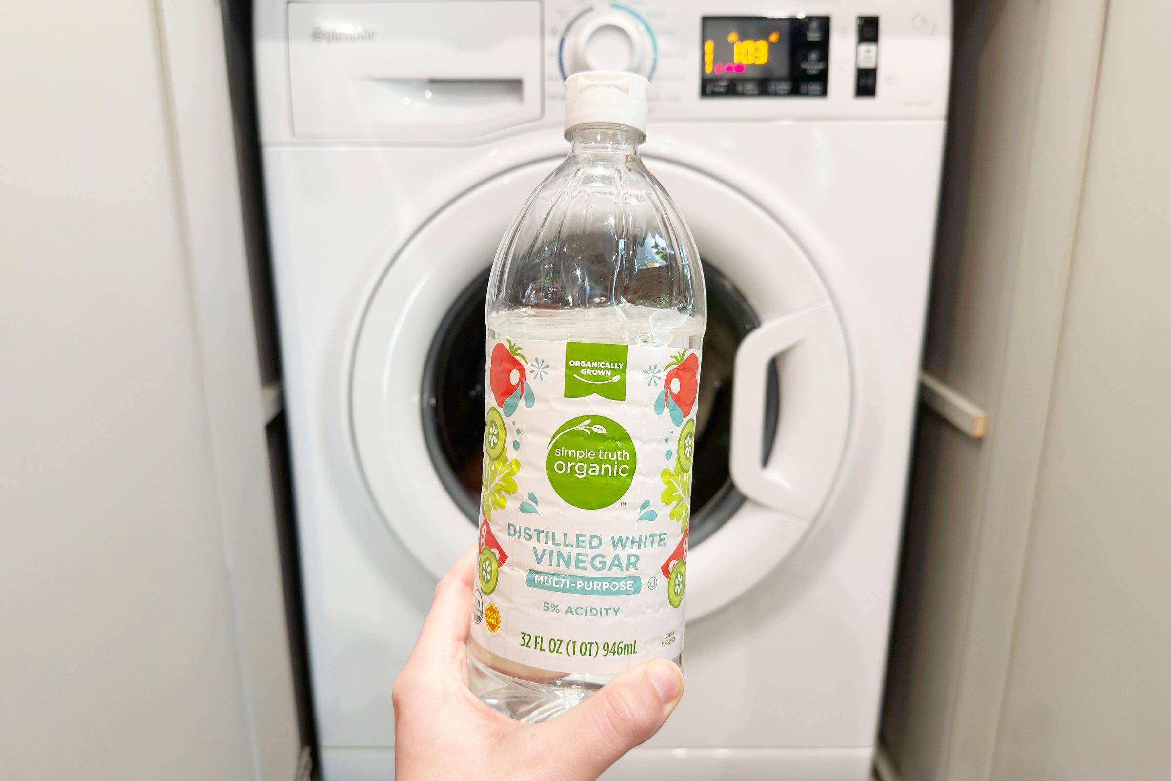 Someone holding up a bottle of vinegar in front of a washing machine.