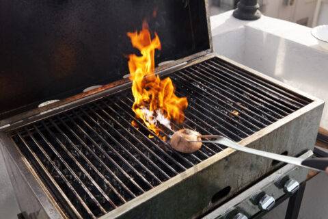 A flaming grill being cleaned with an onion.