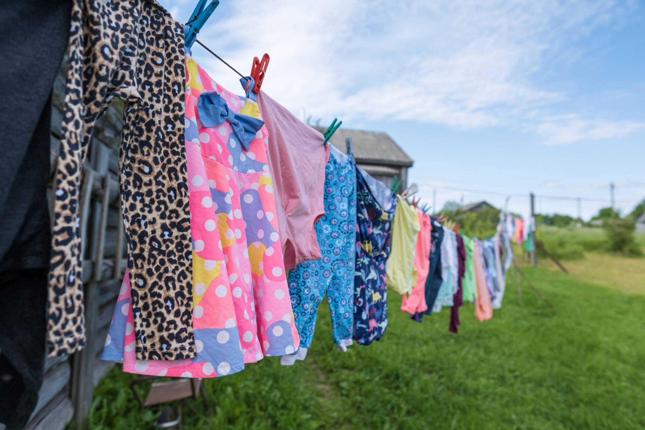 Clean, fresh, bright clothes are dried after being washed in the outdoors, the linen are hung on a clothesline and fastened with clothespins, in the countryside, on a summer day.