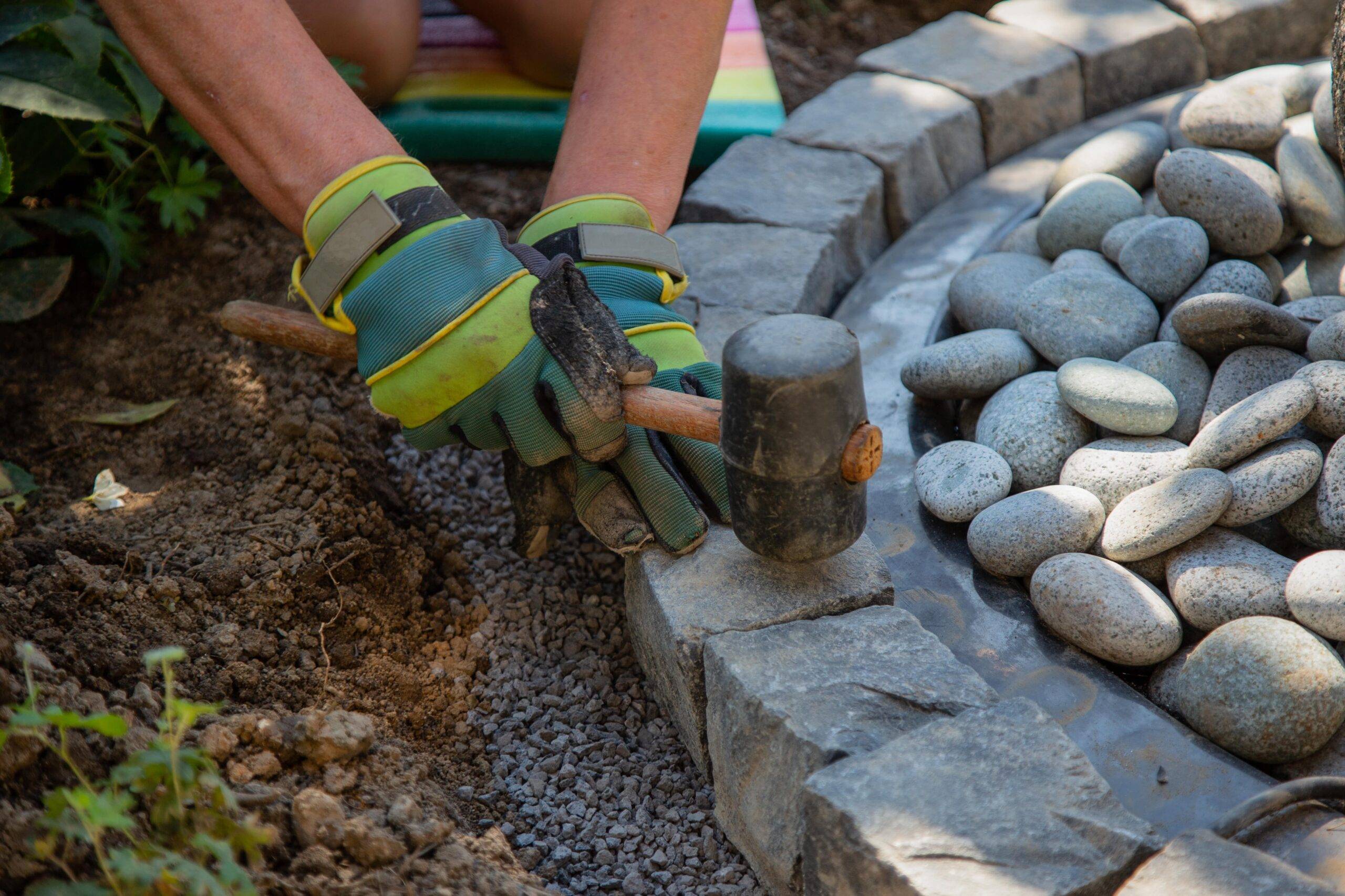 A close view of a landscaper installing a rounded brick border around a garden bed.