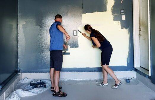 A couple painting a wall dark blue.
