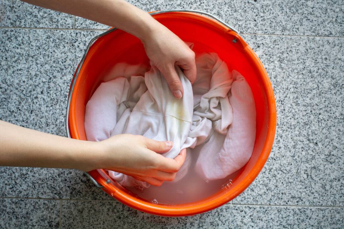 A pair of hands washing clothes in a 5gal bucket.
