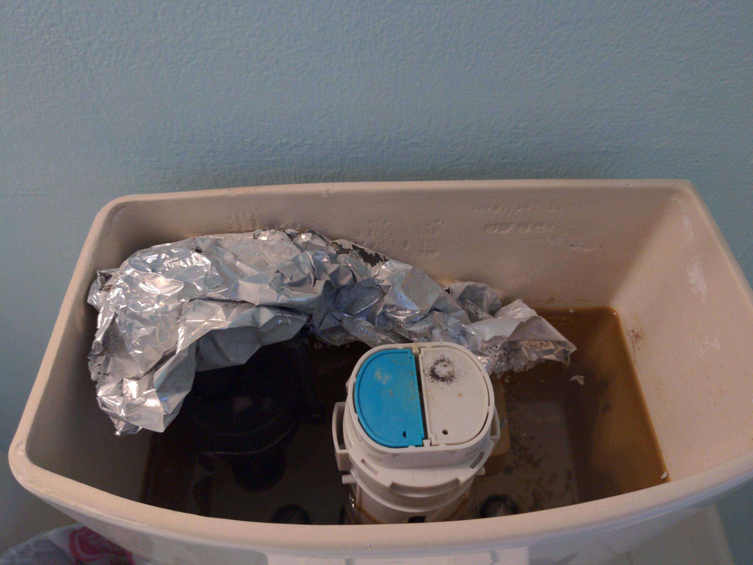 An open toilet tank with a large bunch of aluminum foil in it.