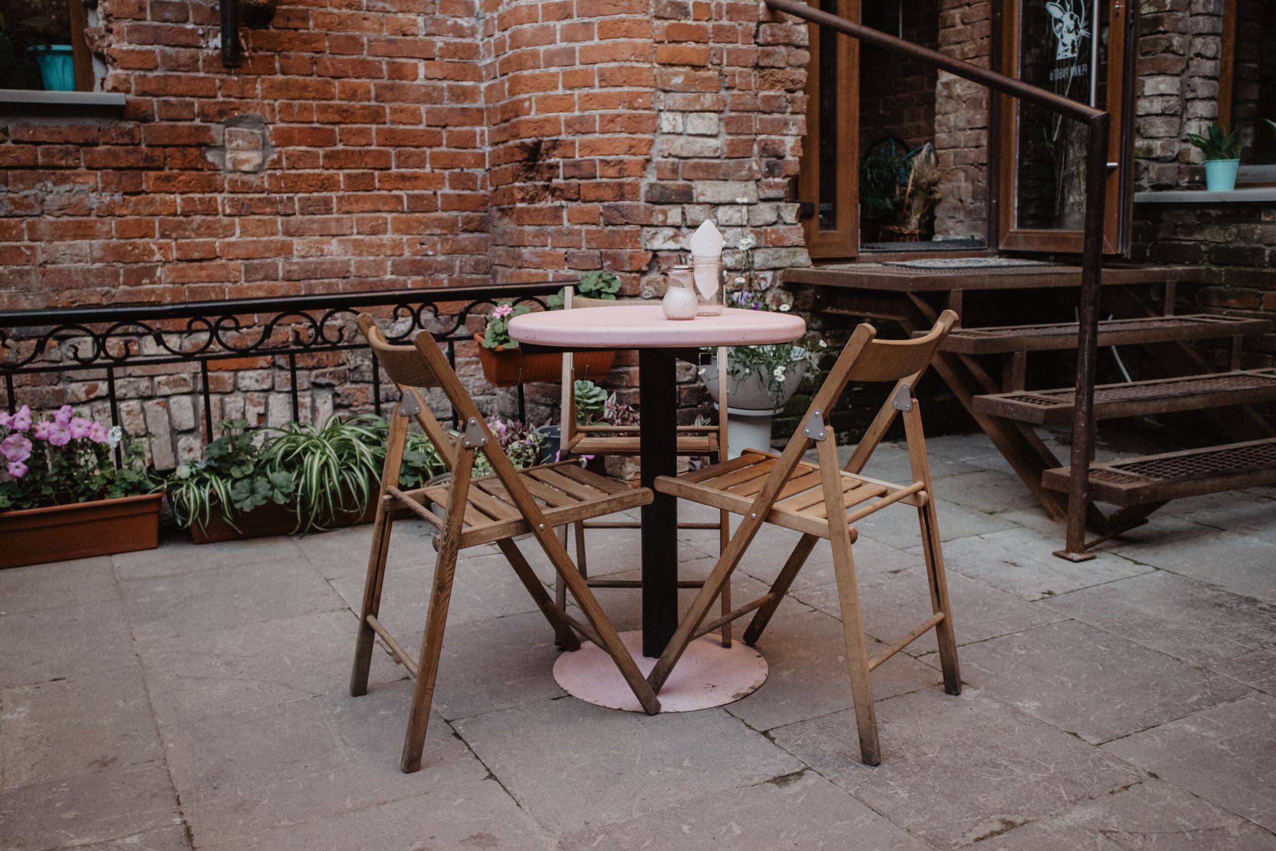 A set of three wooden chairs next to a small patio table.