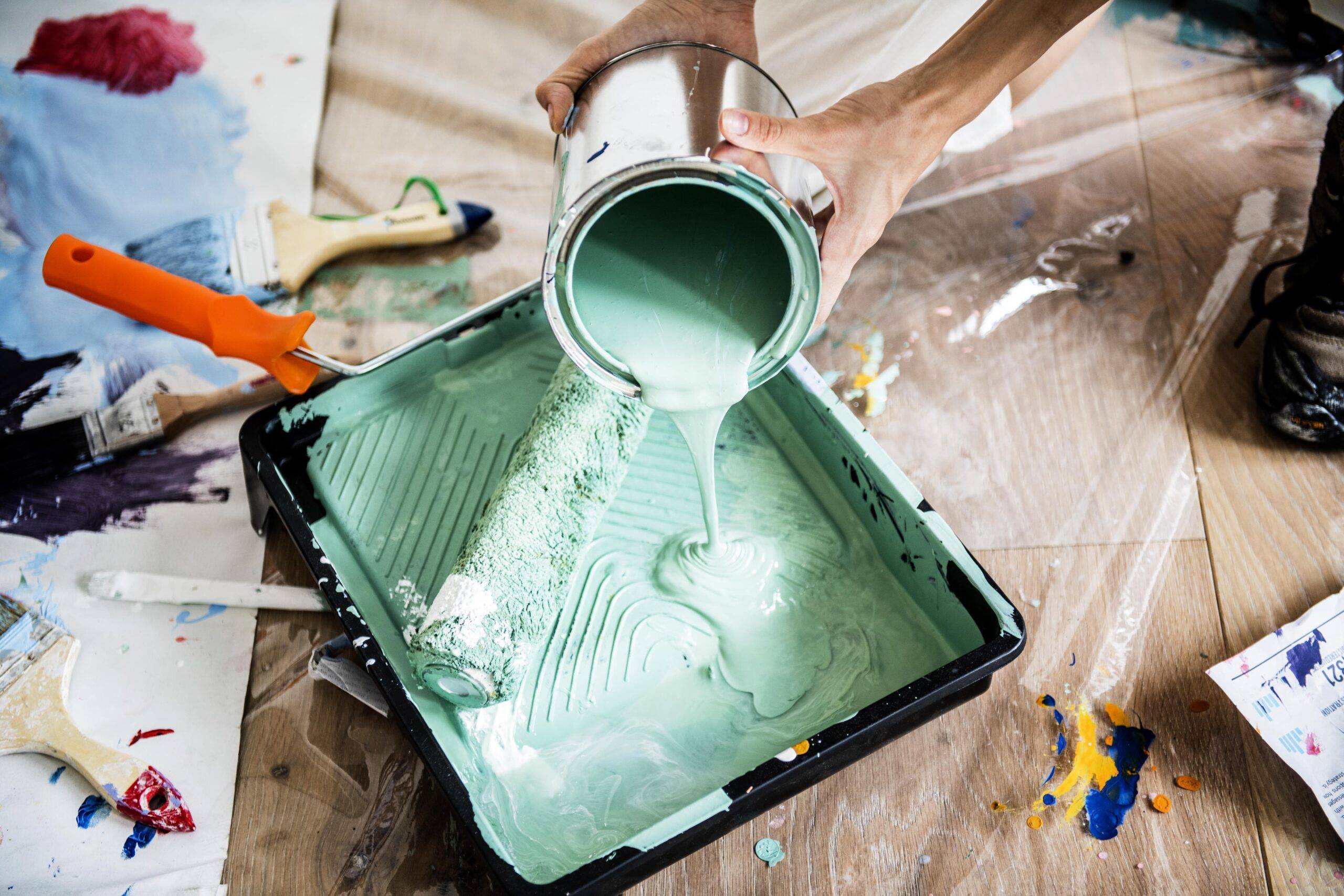 A person pouring a light green paint into a tray.