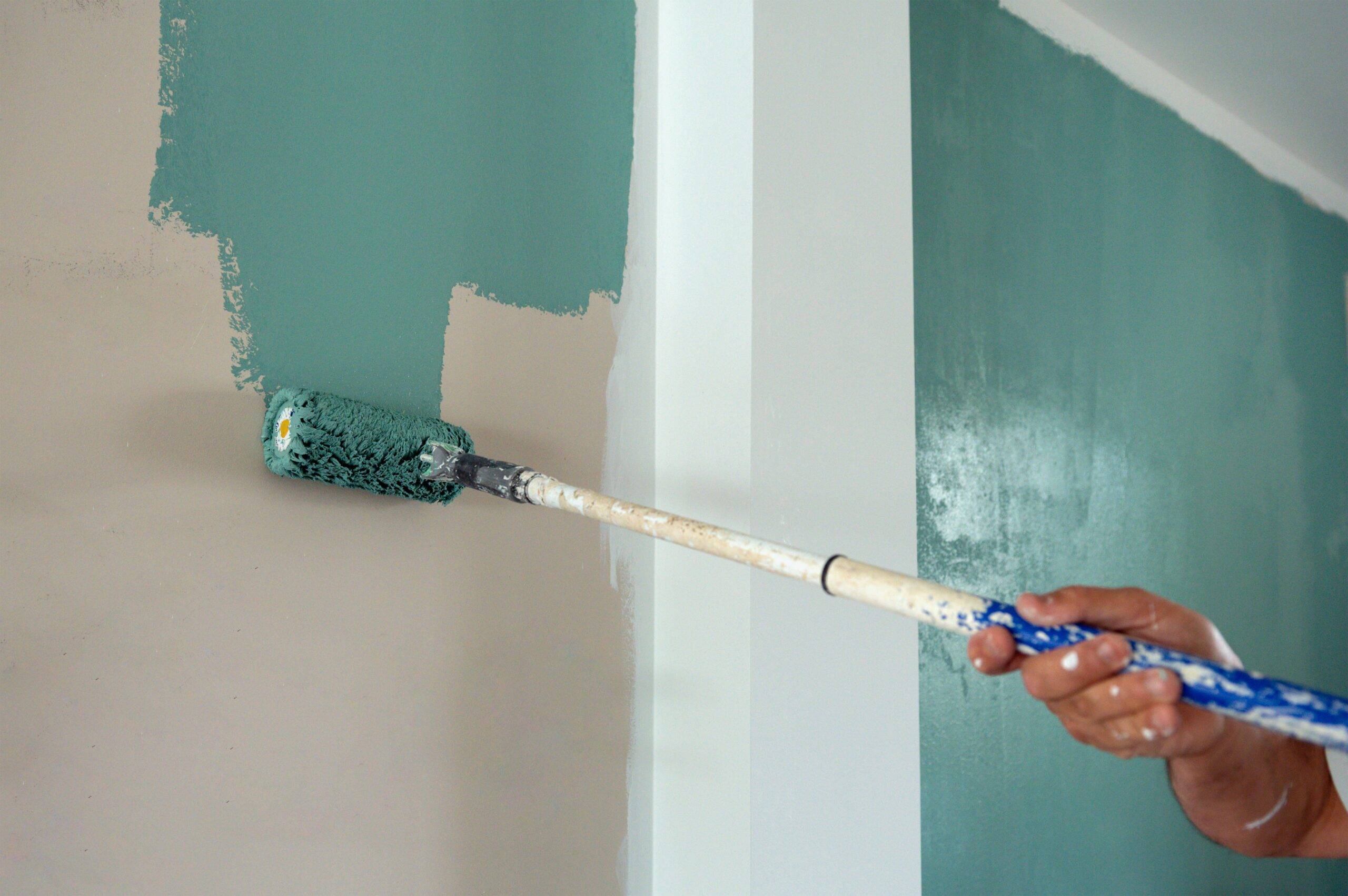 A roller painting a wall a teal color, the person off screen.