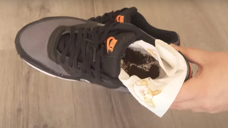 Someone holding up a shoe that contains a paper towel and coffee grounds.