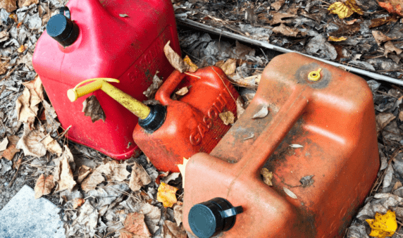 A selection of old gas cans discarded in some leaves.