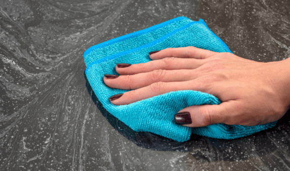 A hand using a bright blue cloth to wipe down a stone counter top.