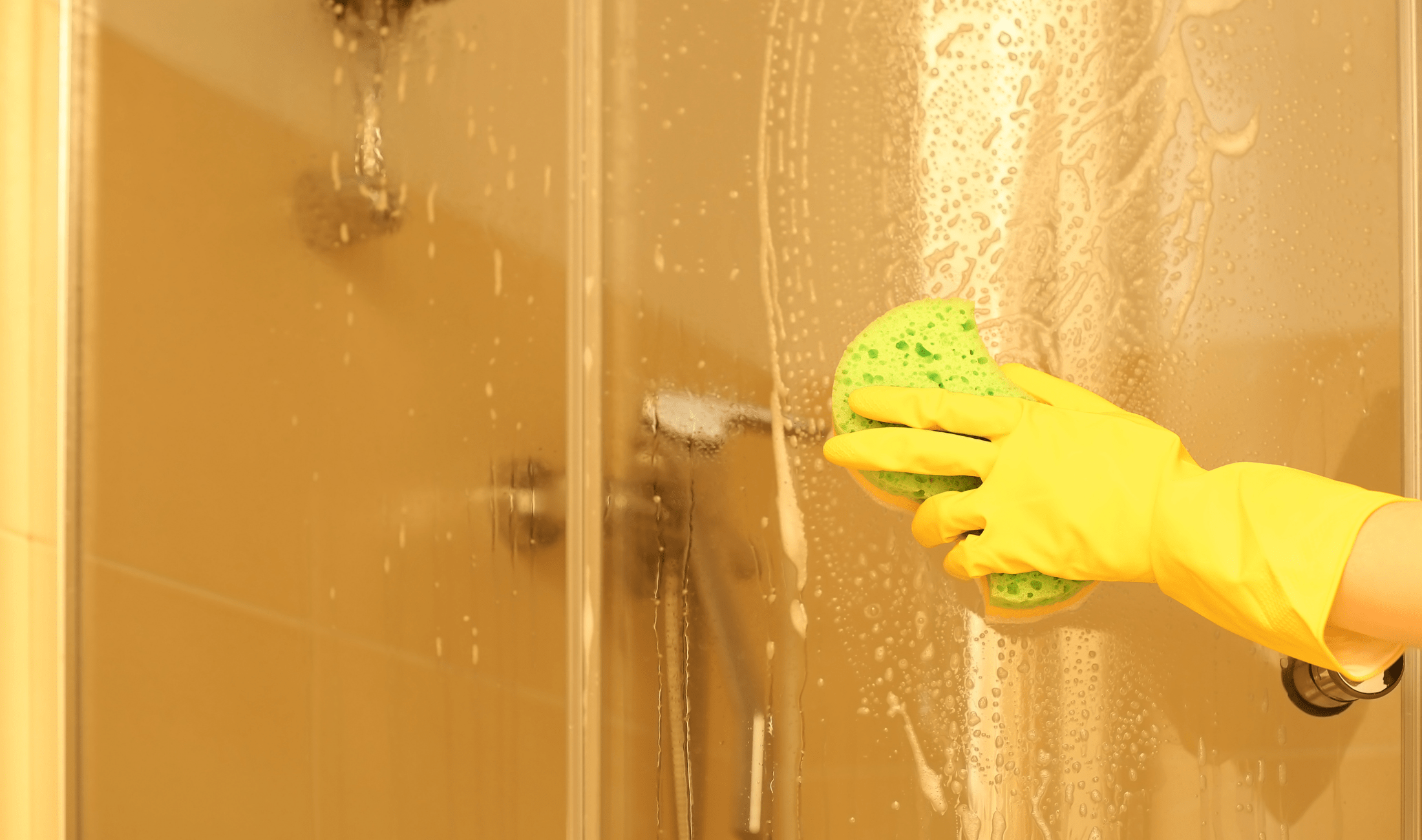A person cleaning a glass shower door with a sponge.