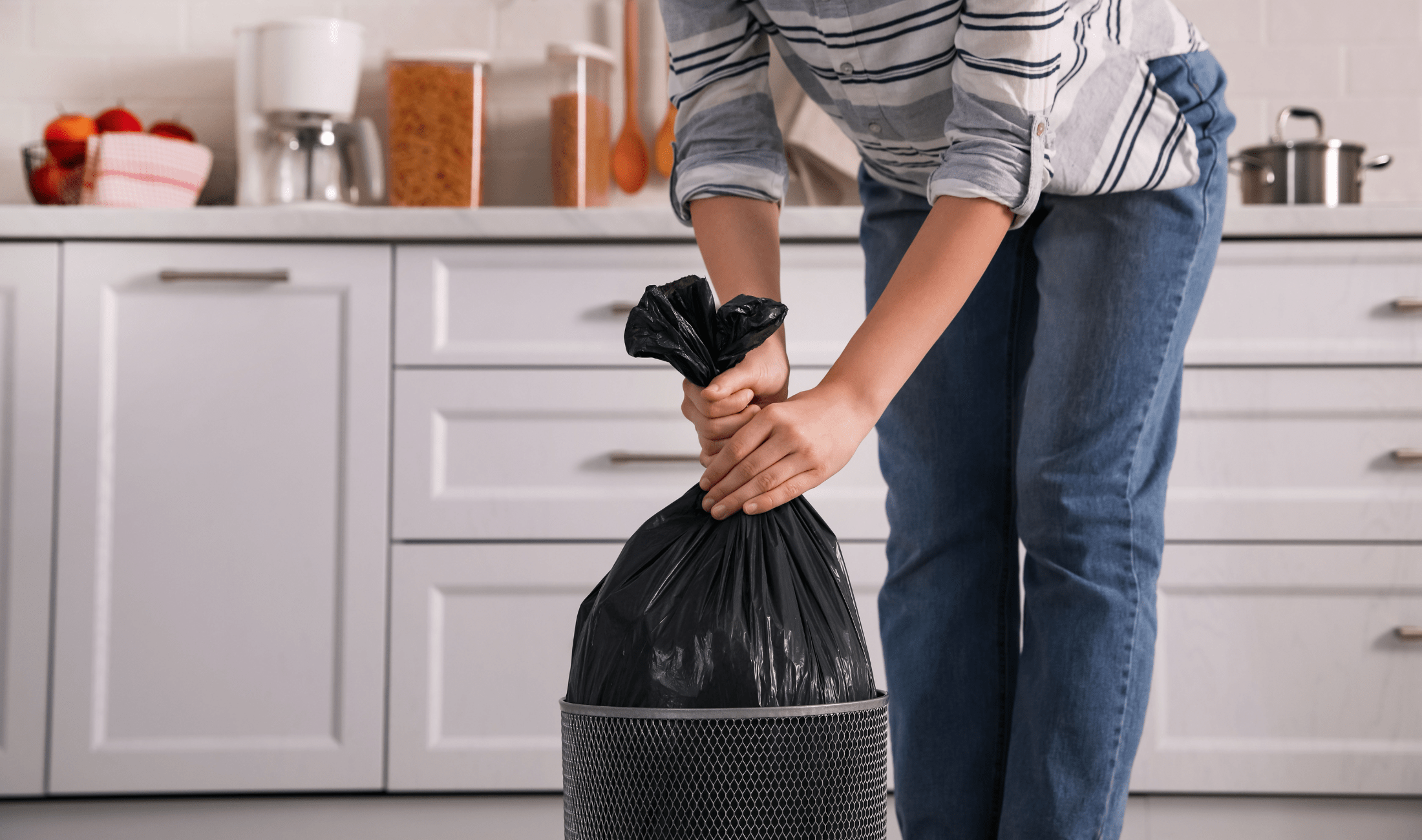 A person picking up a garbage bag out of a garbage bin.