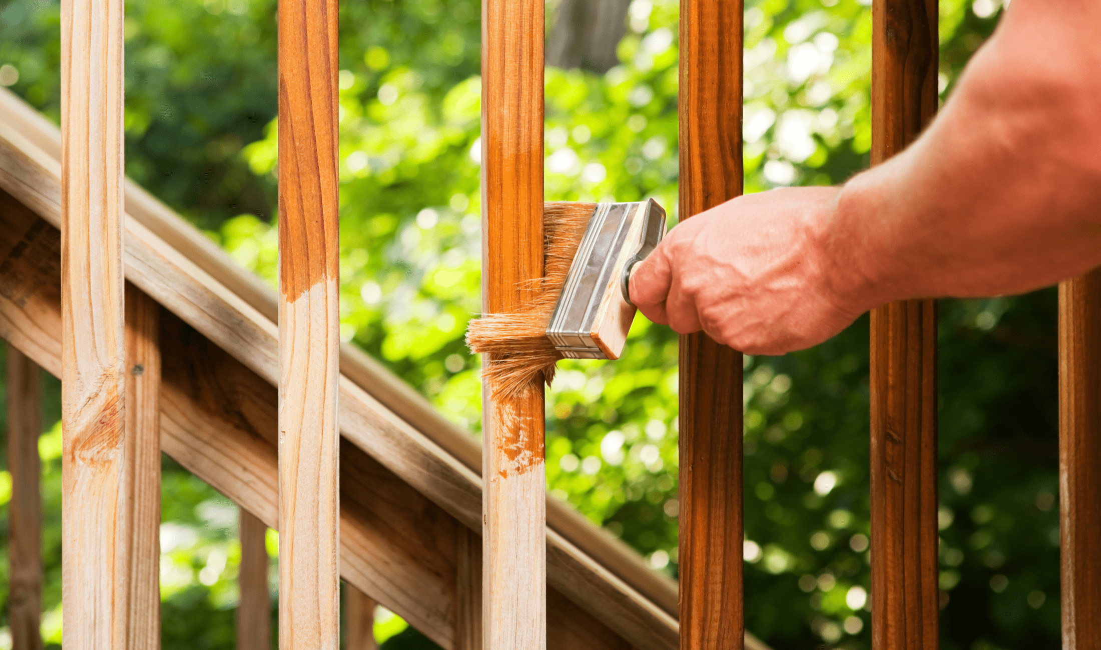 A hand staining the railing of an outdoor deck.