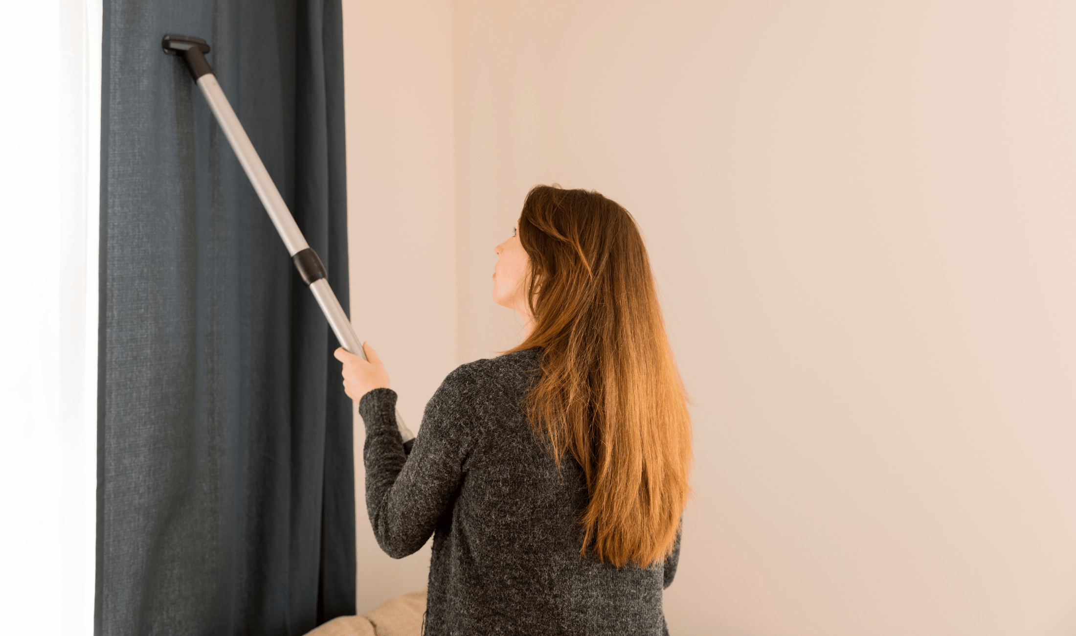A woman vacuuming her curtains.