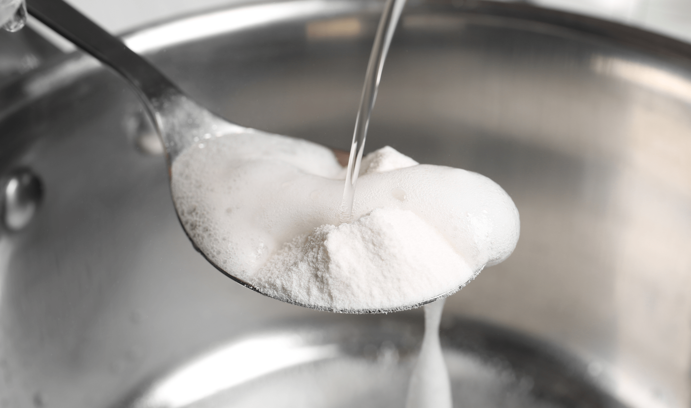 A spoonful of baking soda with water being poured on it, causing it to fizz.