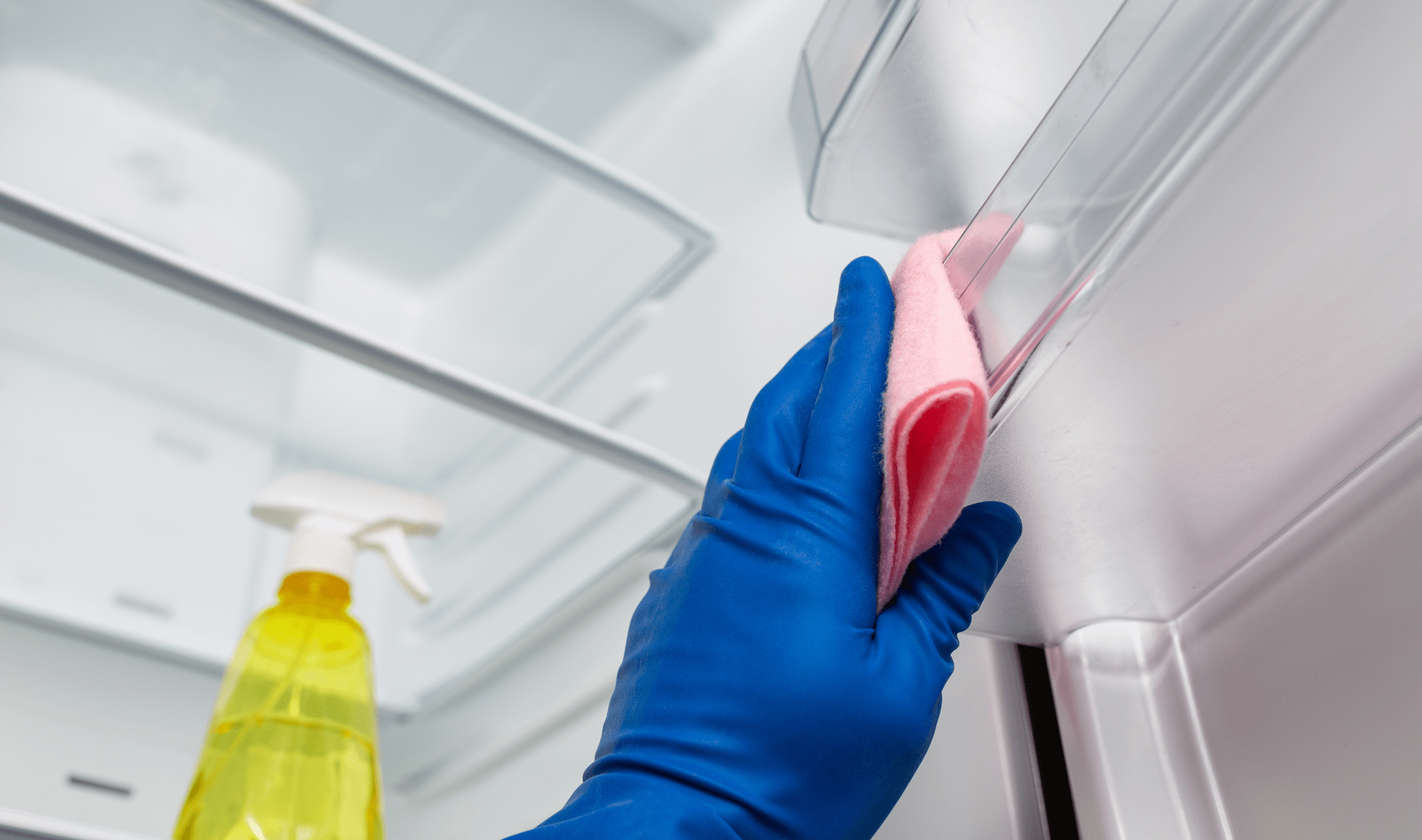 A low-angle shot of a gloved hand wiping the inside of a fridge.