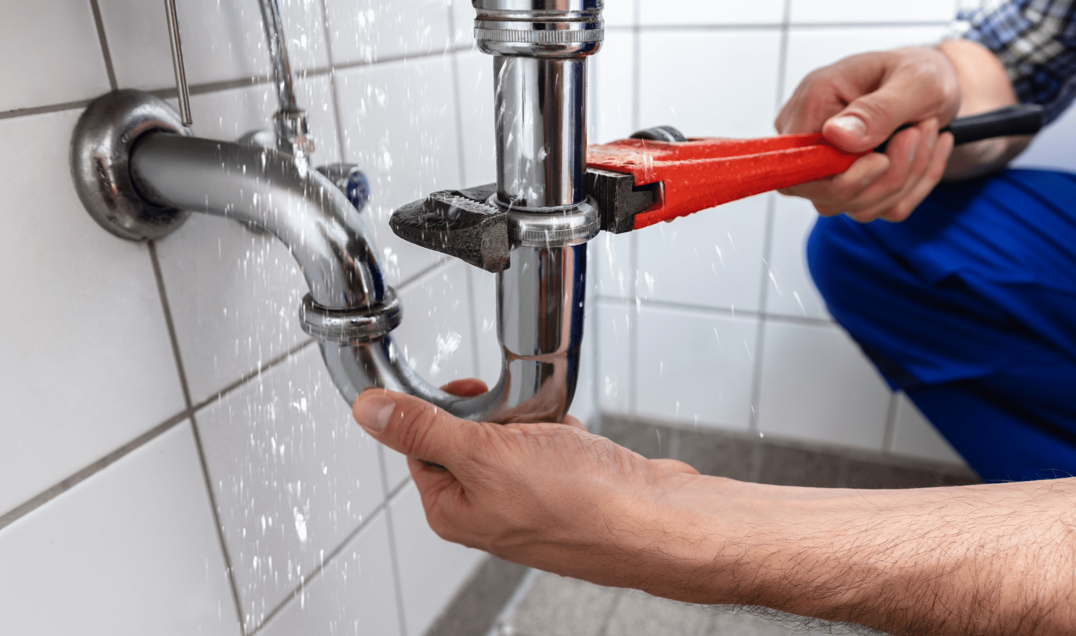 A person holding a large wrench tightening a leaking pipe.