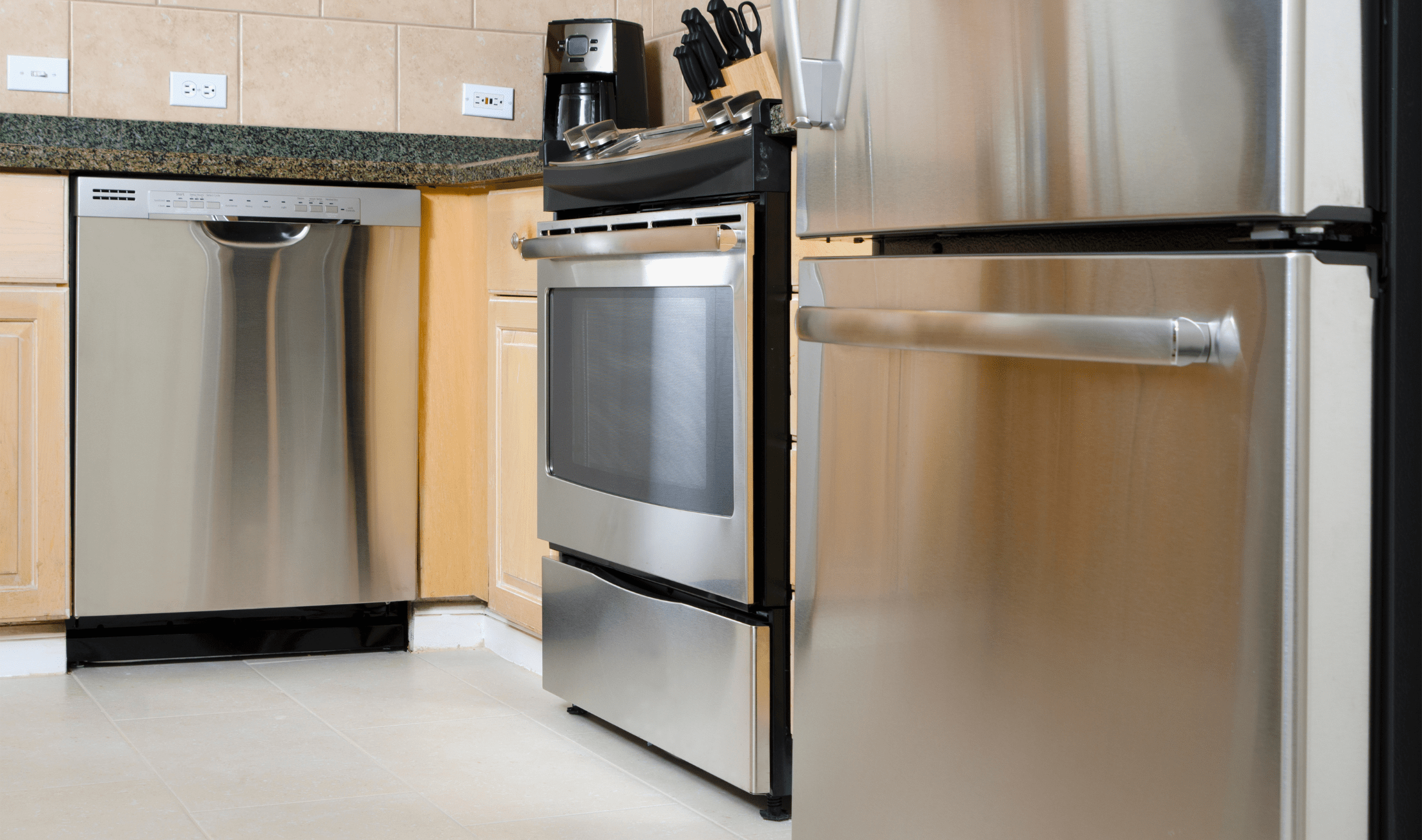A low-angle shot of a kitchen with a stainless steel fridge, stove, oven, dishwasher, and coffee machine, all within proximity of each other.