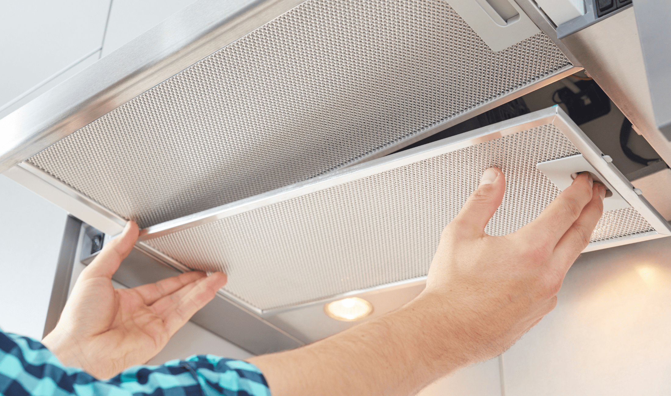A pair of hands removing the filter off the bottom of a range hood.
