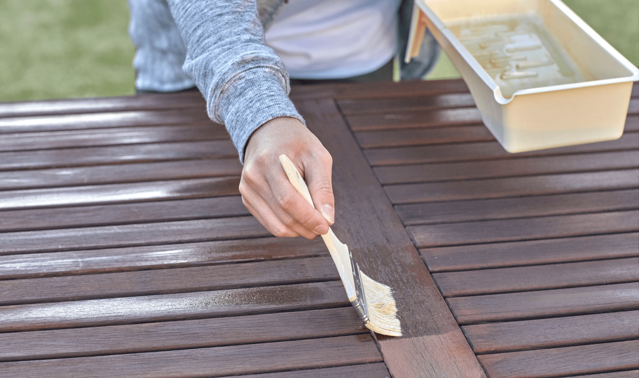 A person painting their outdoor table with wood varnish.