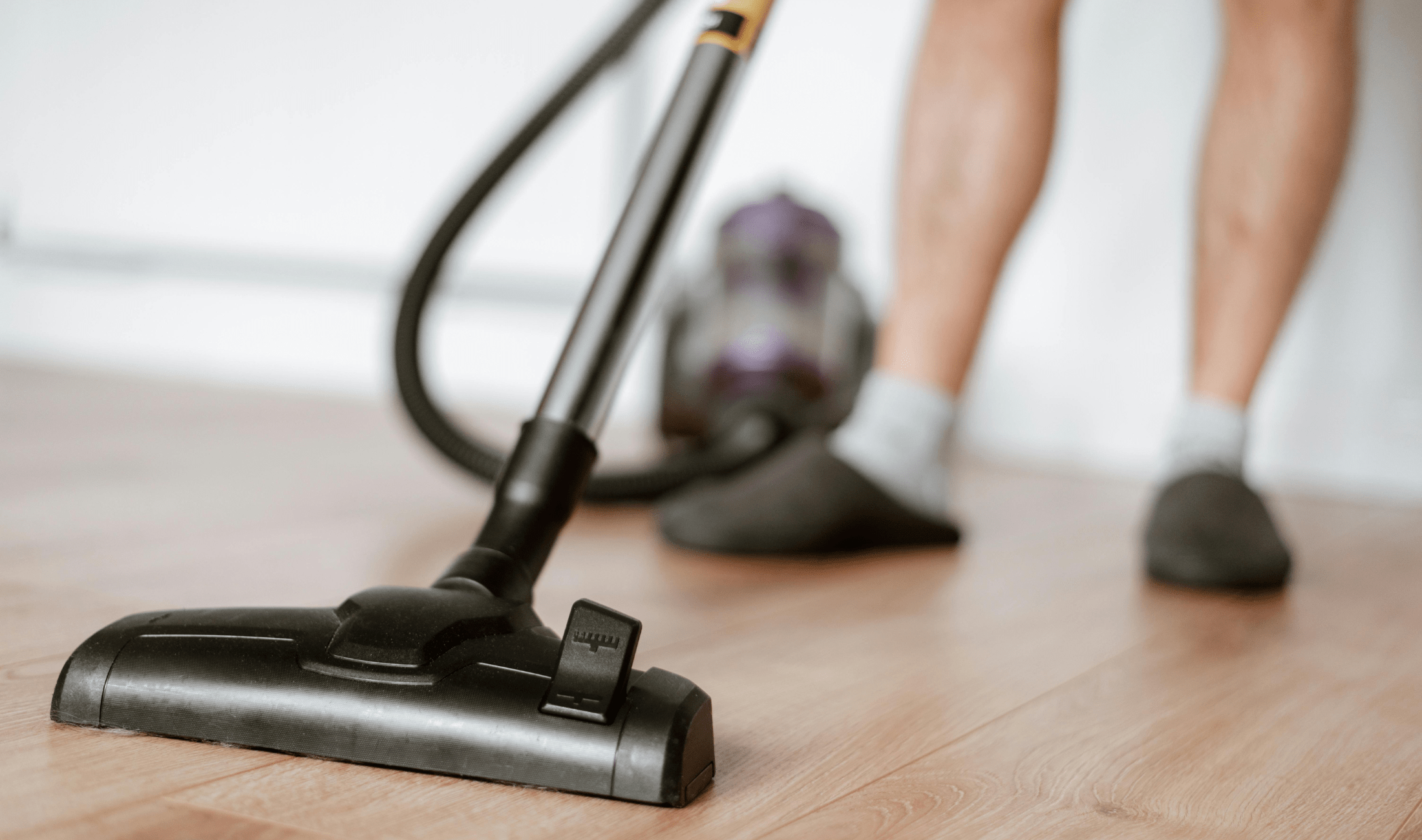 A low shot of someone using a vacuum on their hardwood floor.