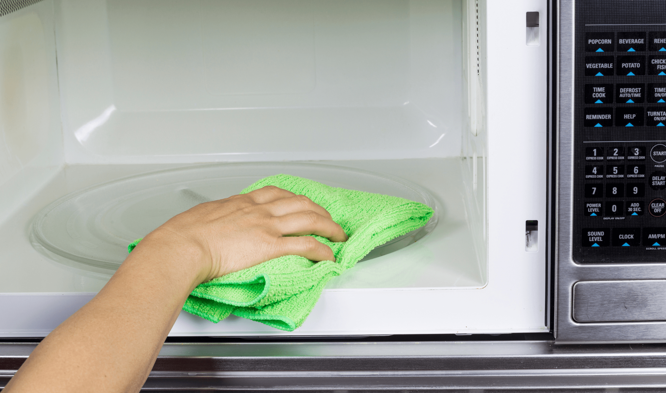 A hand holding a microfiber cloth wiping the inside of a microwave.