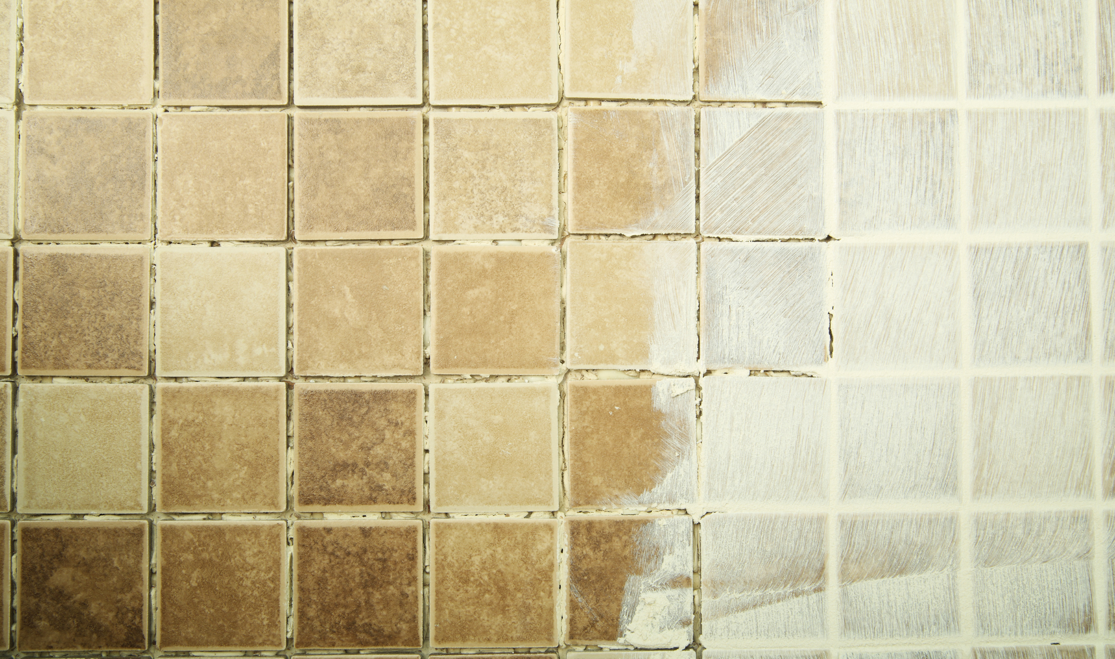 A tiled bathroom wall, half dirty, half clean.