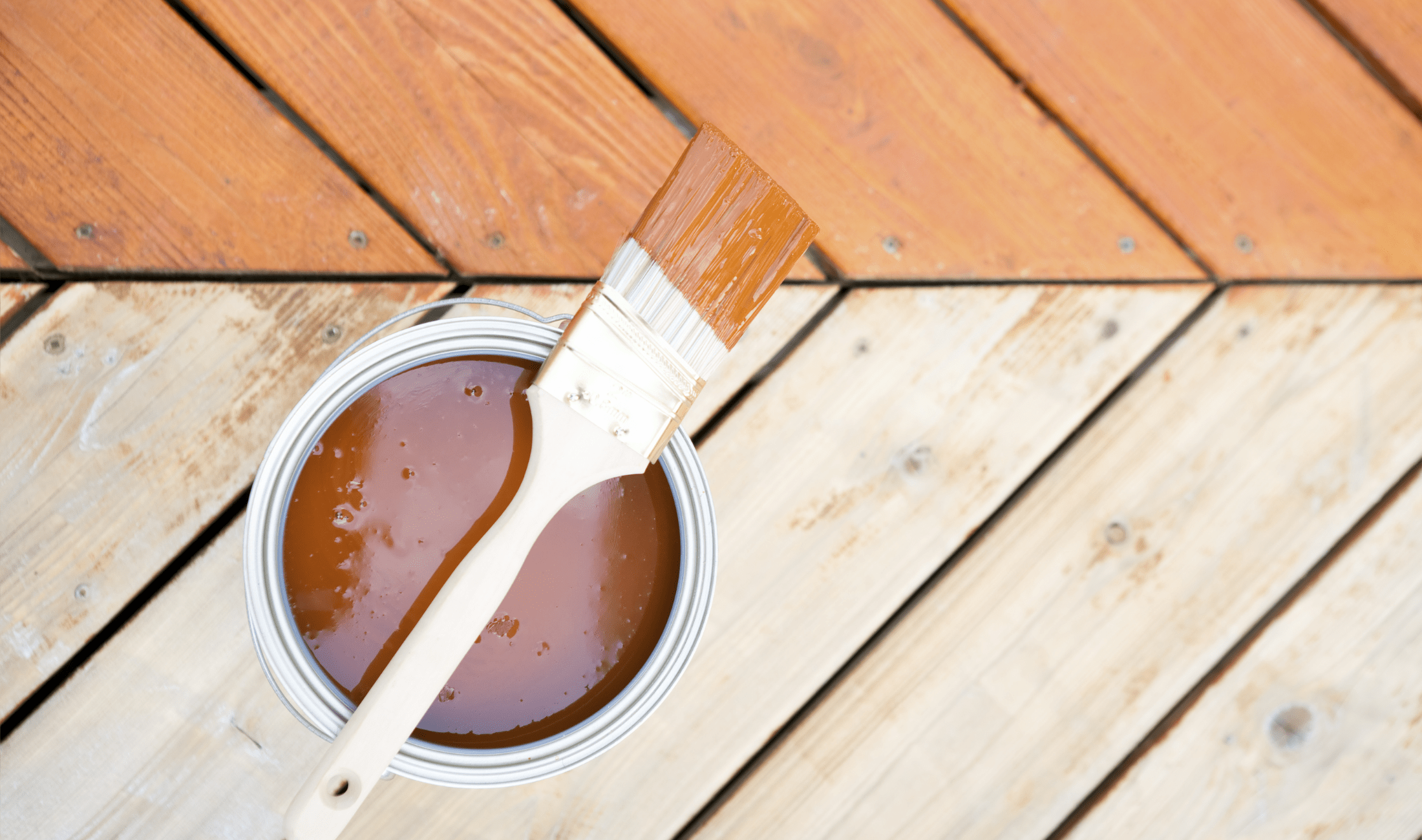 An aerial view of an outdoor deck, half stained, half untreated, a can of stain with a brush on top visible.
