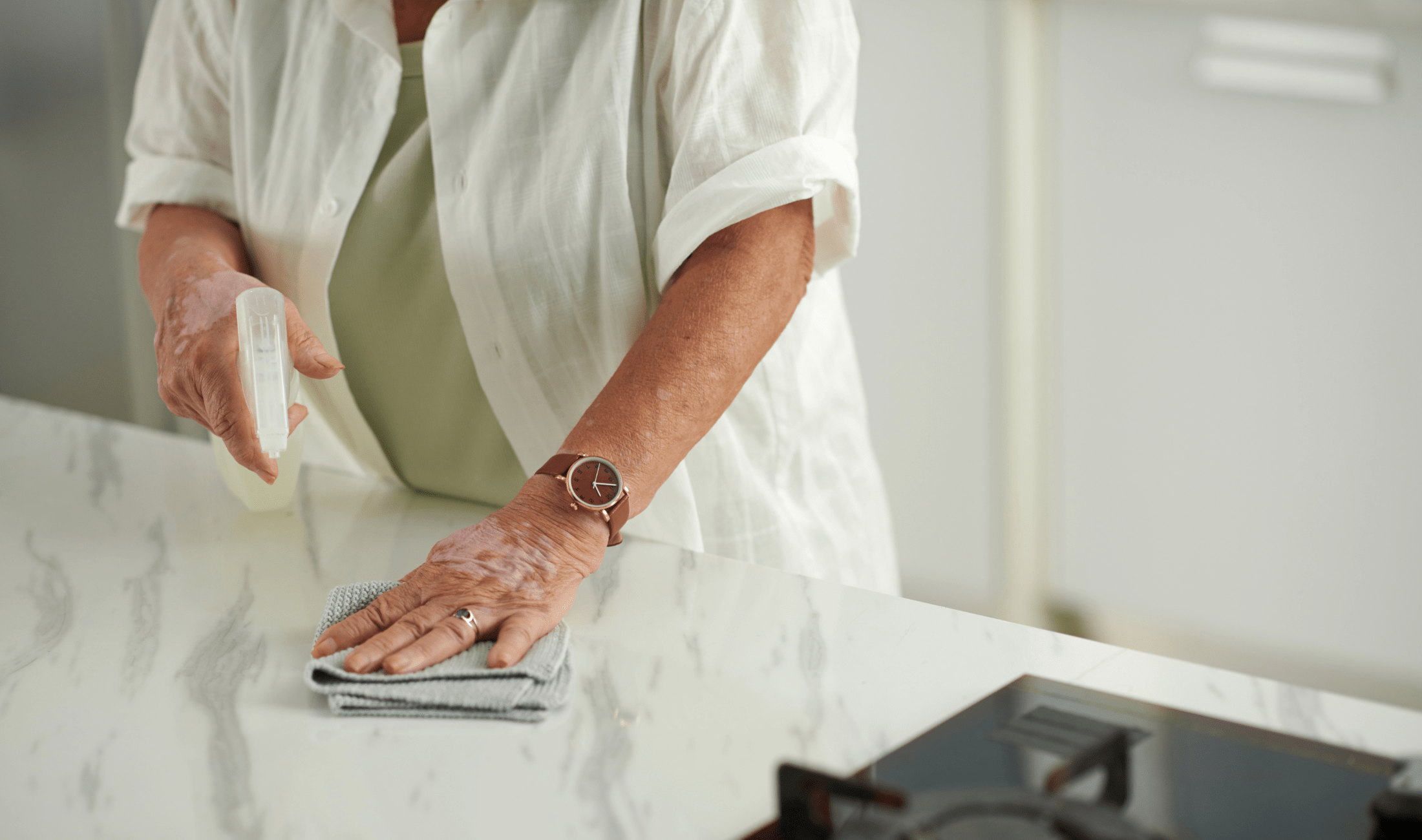 A person spraying their kitchen counter with a cleaner before wiping it off.