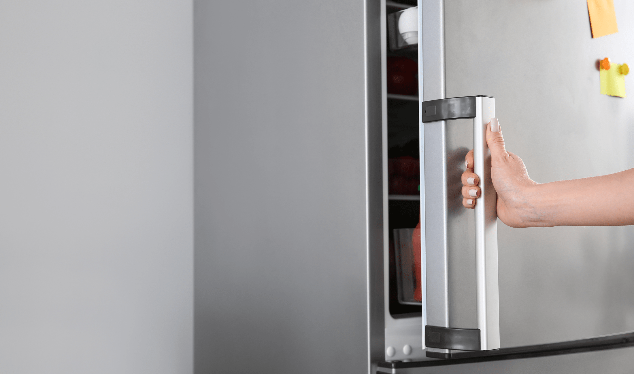 A hand opening a stainless steel fridge door.