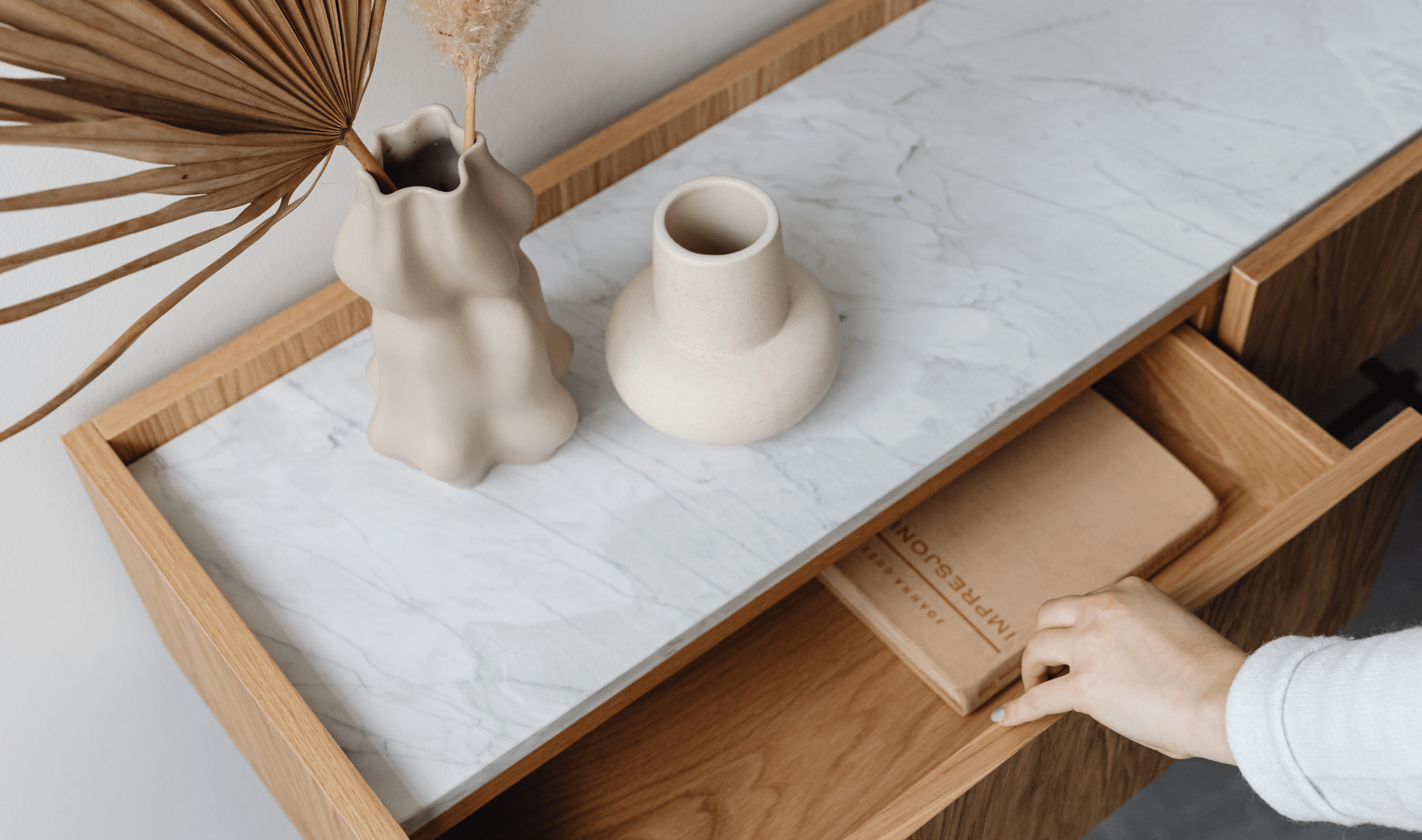 A minimalist side table with a hand opening one of the drawers.