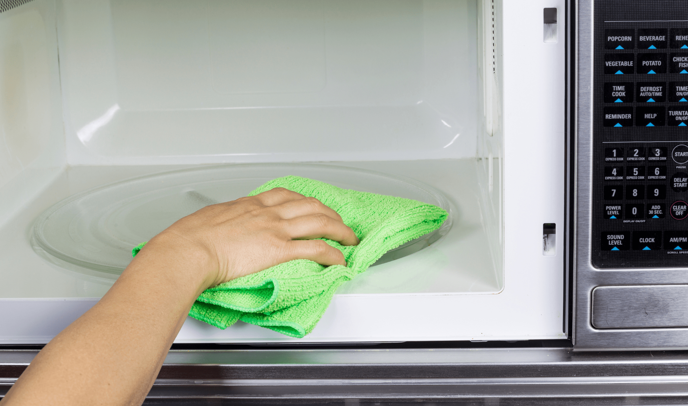 A hand with a cloth wiping the inside of a microwave.
