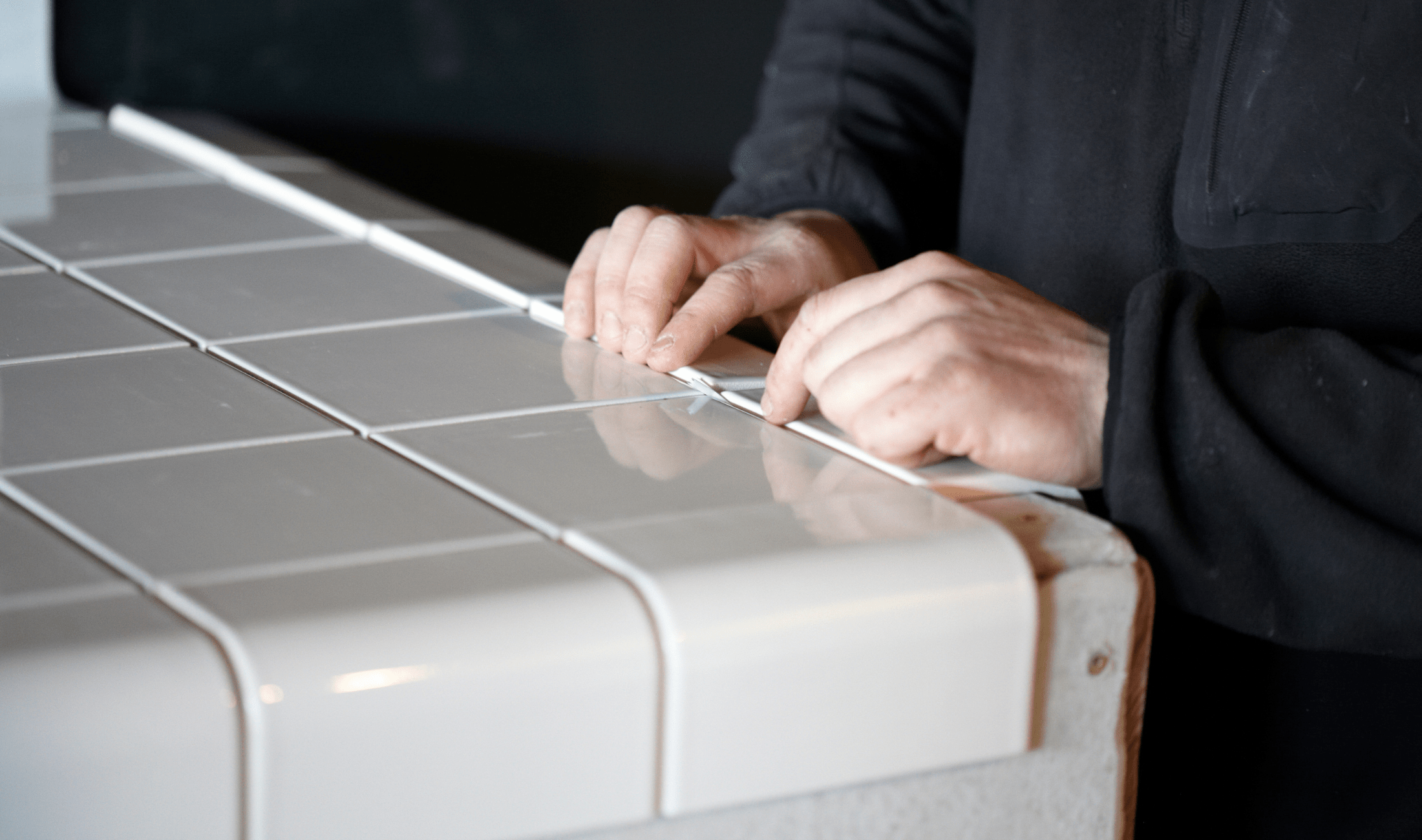 A pair of hands laying white tile for a tile countertop.