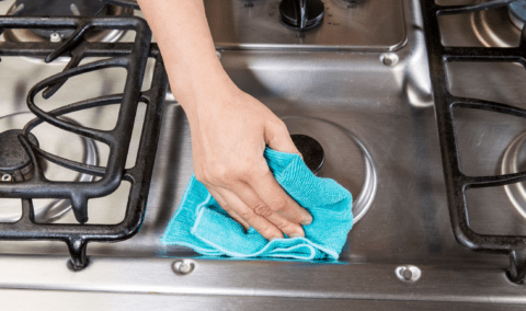 A hand with a cloth wiping down a stainless steel stove.