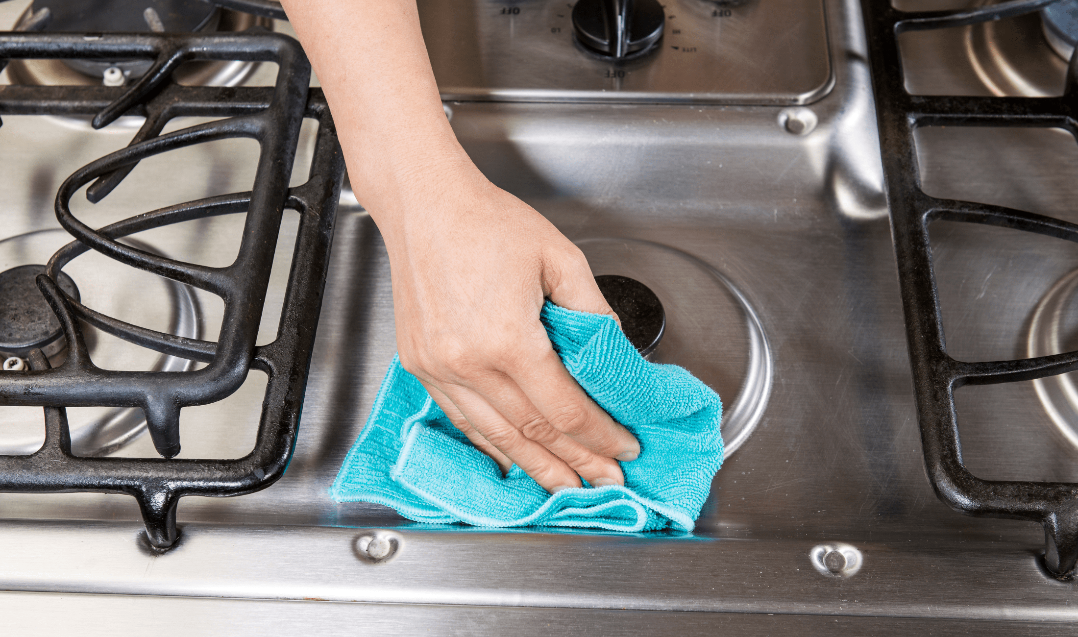 A hand with a cloth wiping down a stainless steel stove.