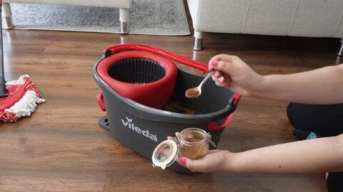 A person scooping a spoonful of cinnamon into a mop bucket.