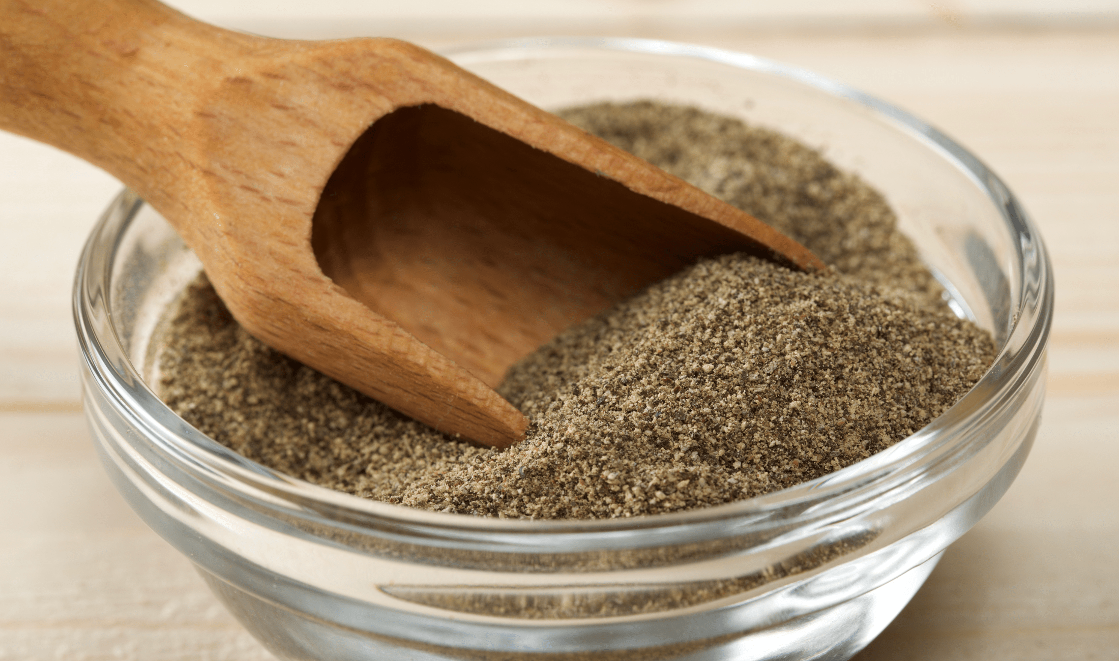 A wooden scoop in a bowl of ground pepper.