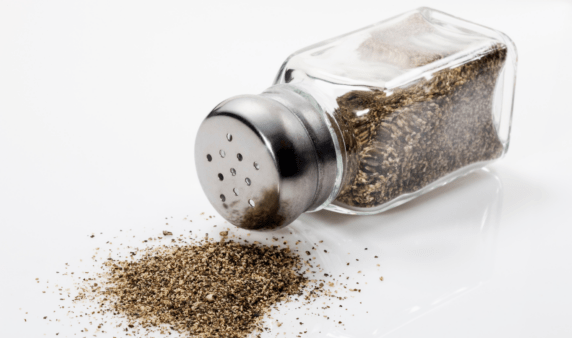 A pepper shaker that's been knocked over, having spilled on the white surface beneath.