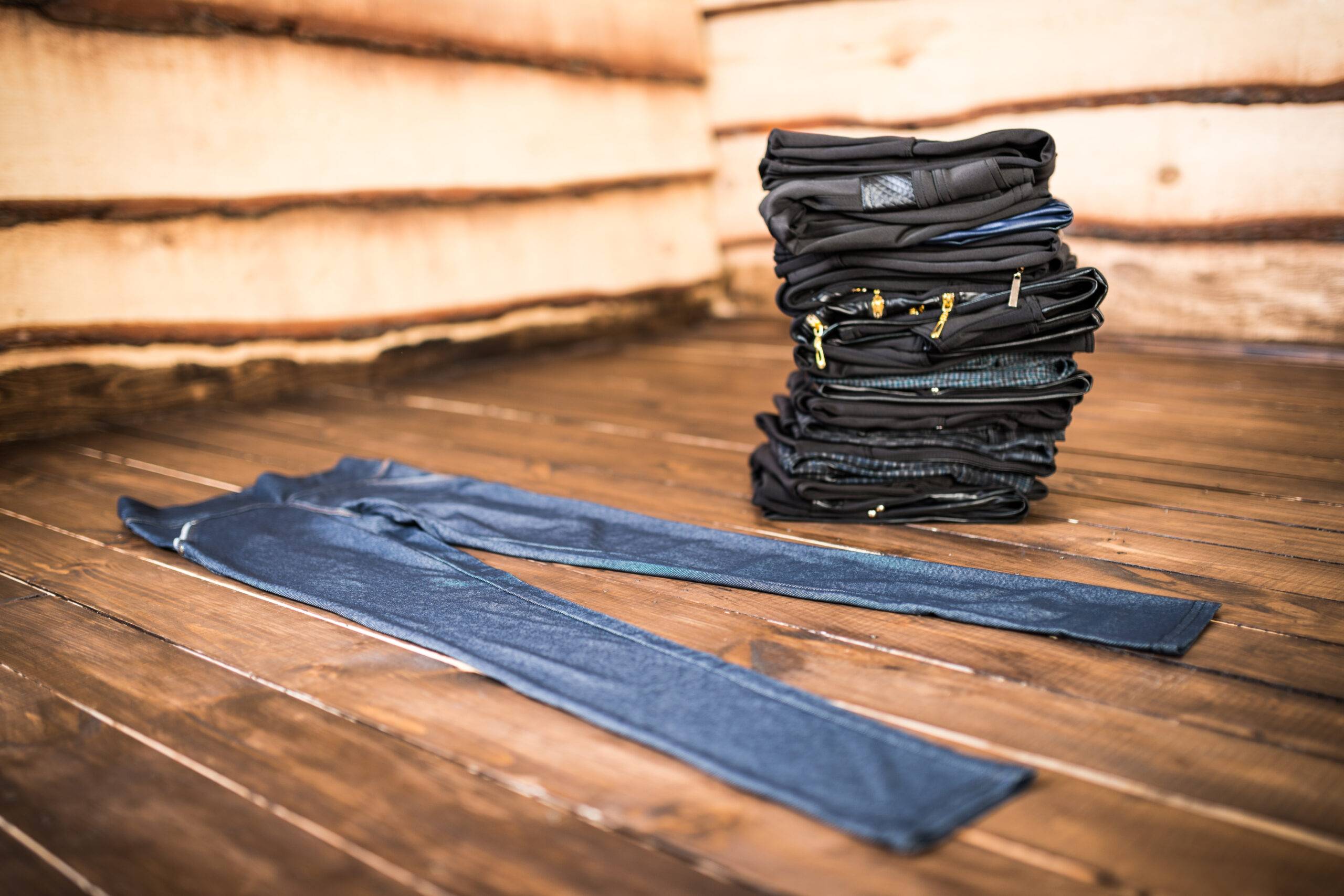 Black women's trousers lie against the background of a pile with dark things lying on a wooden floor. The concept of everyday monotonous wardrobe
