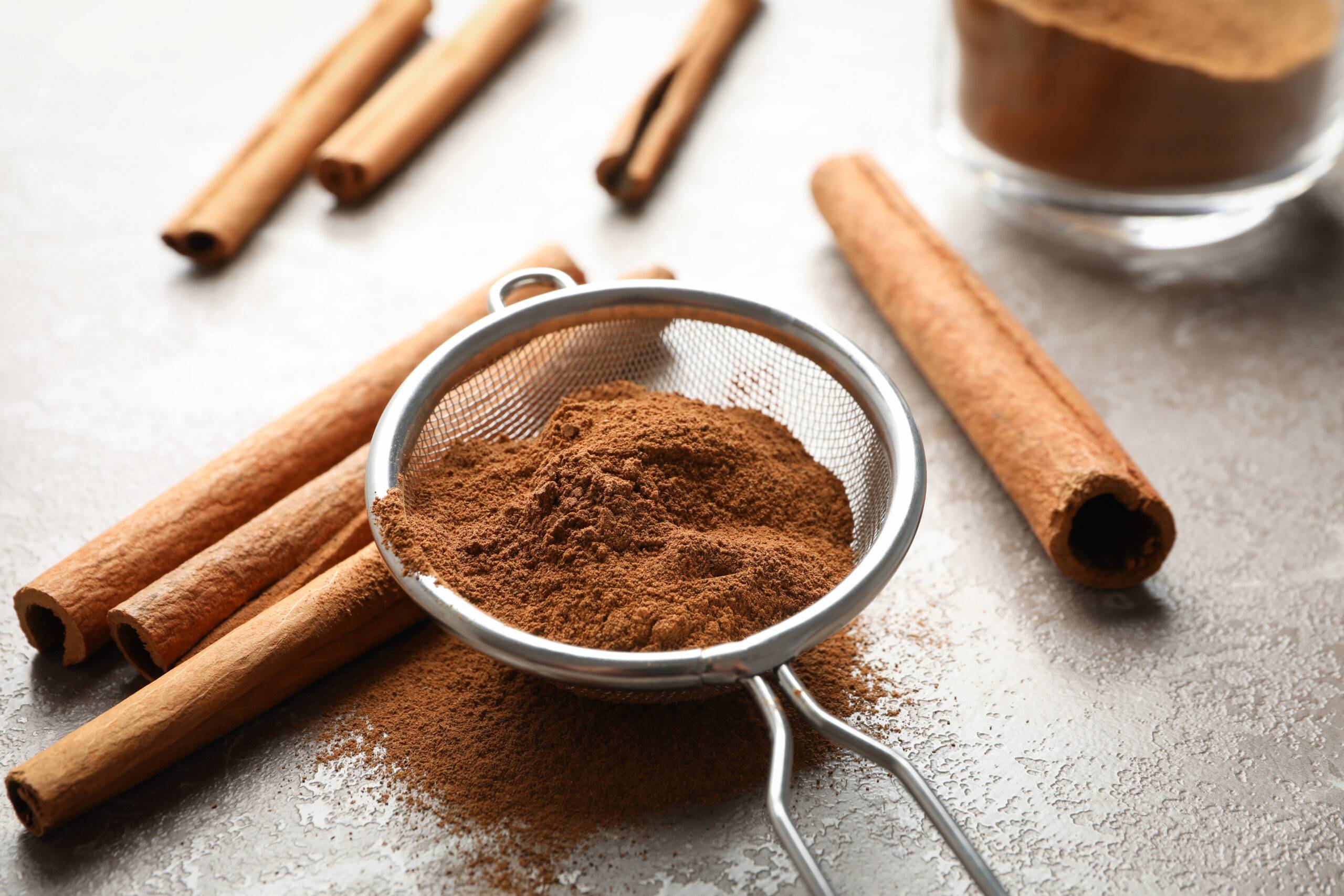 Cinnamon sticks, powder and sieve on grey background, space for text